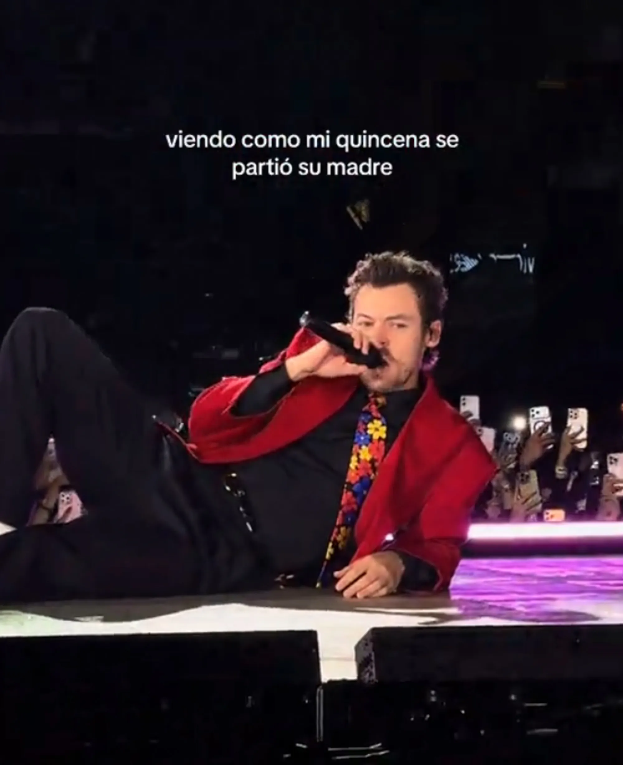 Harry Styles laying on his back on stage, holding a microphone.