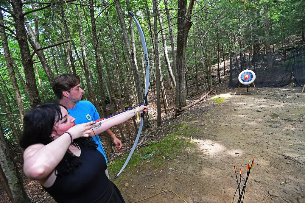Archery instructors Steven Blacher and Thomas Gray help camp-goer Marissa Matozzo learn to hit the target.