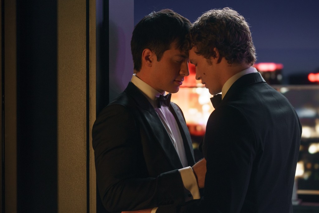 Two men in tuxedos, Hudson Williams and Connor Storrie, forehead to forehead in a tender moment.