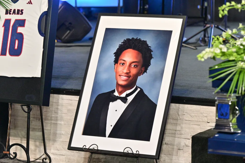 A framed portrait of Nolan Wells at his funeral, next to a white jersey with "BEARS 16" on it.