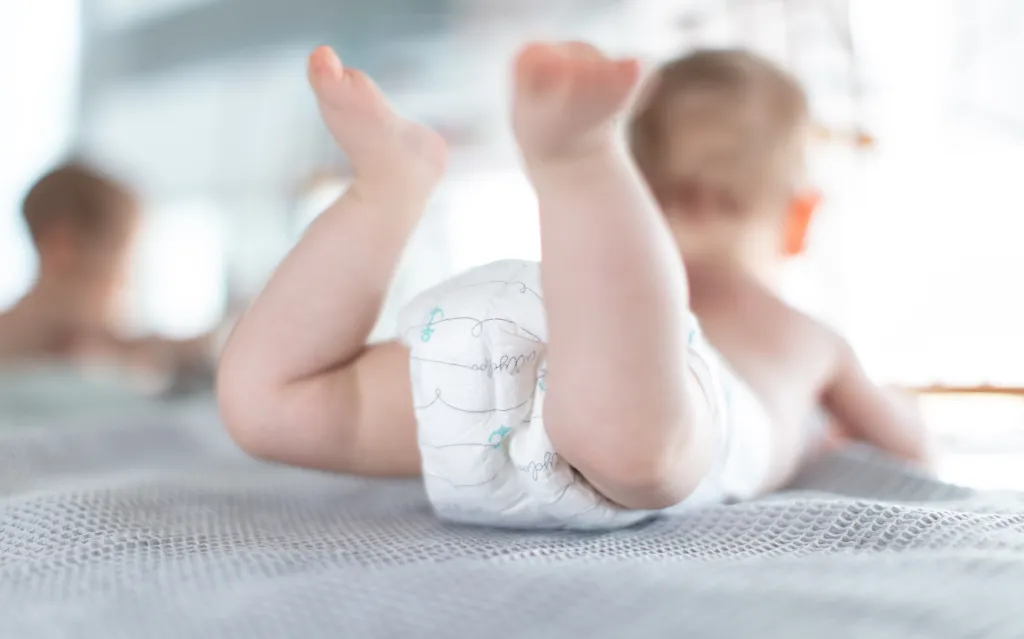 An infant wearing a diaper and lying on its stomach on a light blue patterned blanket.