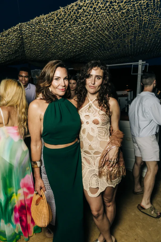 Two women, one in a green halter dress and the other in a crochet dress, standing together at an event.