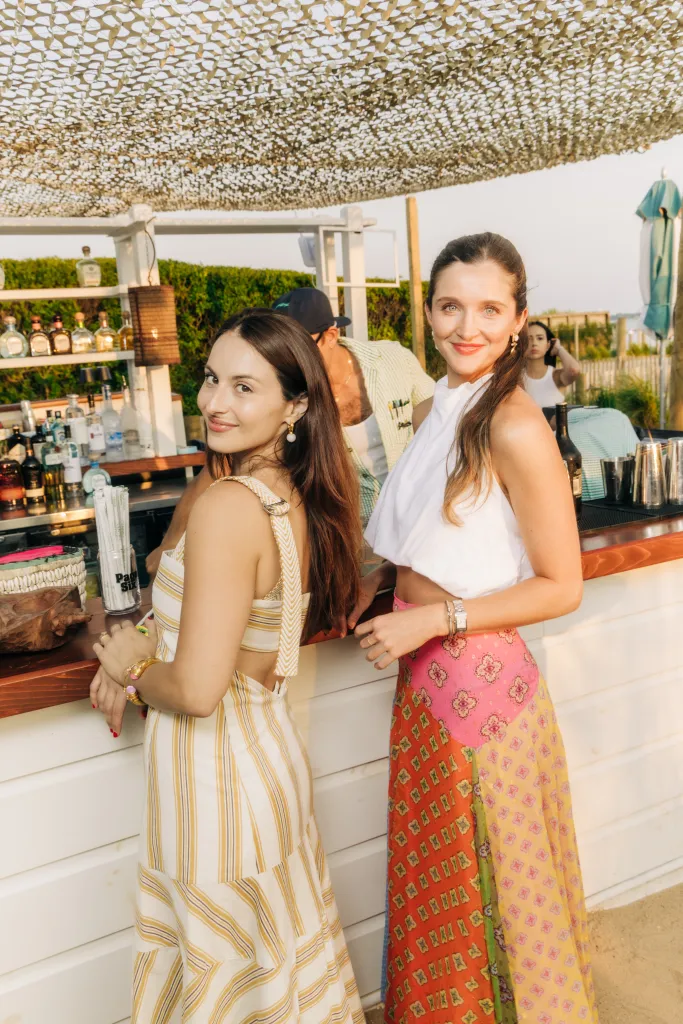 Two women smiling at a bar at the Page Six's VRT Out East Party.
