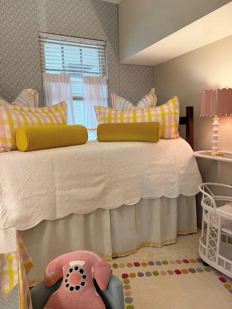 A dorm room with a bed covered in a white quilt, yellow pillows, and a pink telephone-shaped pillow.