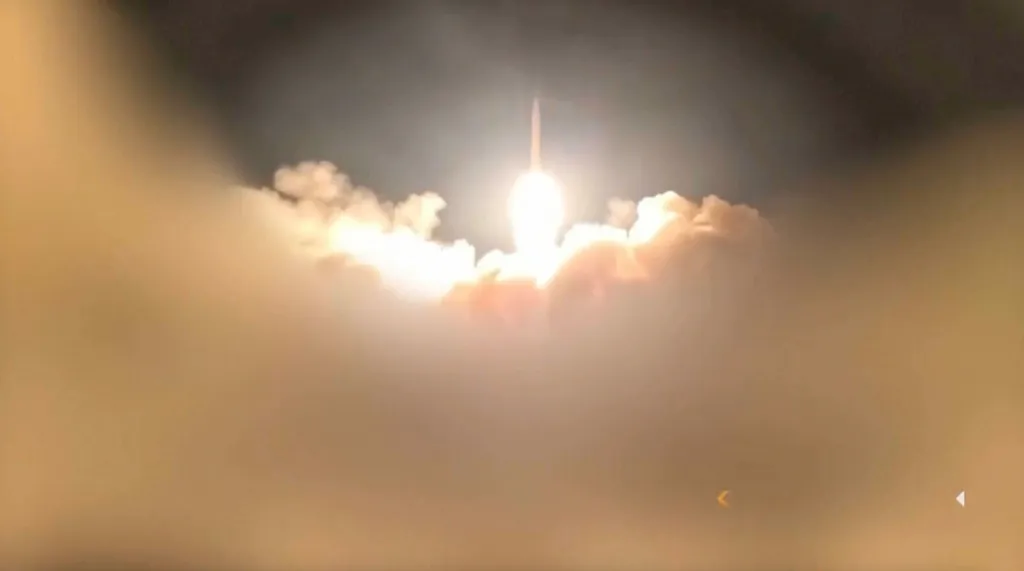 Missile launch illuminating the night sky and surrounded by smoke.