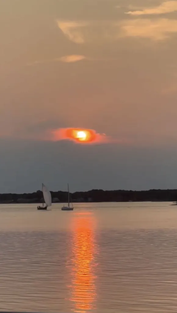 Two sailboats on a calm body of water with an orange sunset reflecting on the surface.