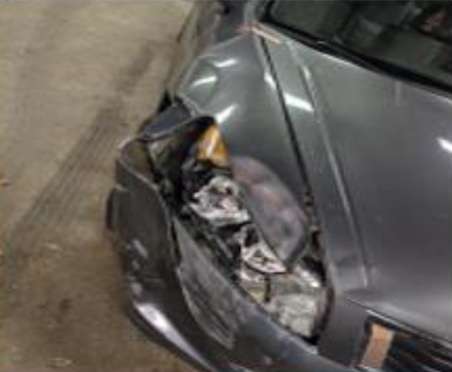 A gray car with significant damage to its front passenger side, including a crumpled fender and shattered headlight.