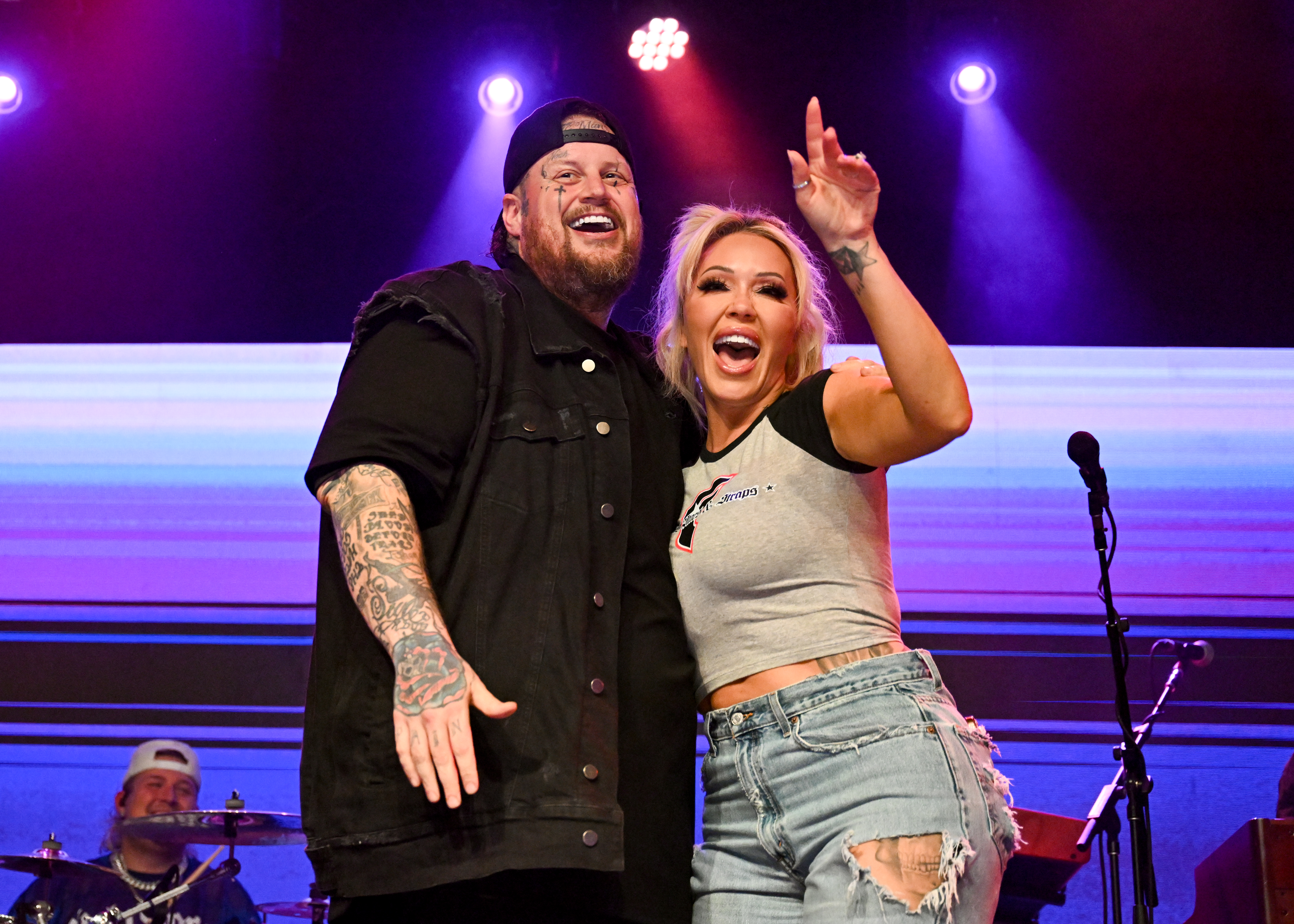 Jelly Roll and Bunnie Xo smiling and gesturing to the crowd at the Jelly Roll & Friends concert.