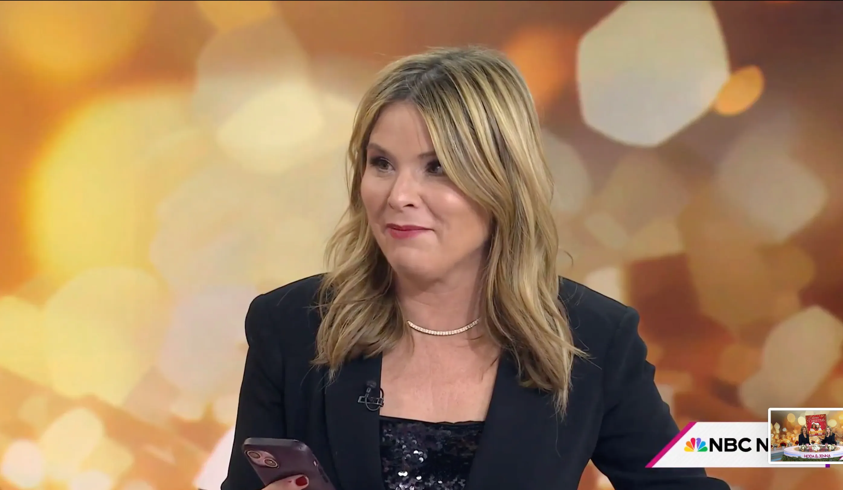 Jenna Bush Hager holding a phone, with a small screen of her show visible in the bottom right corner.