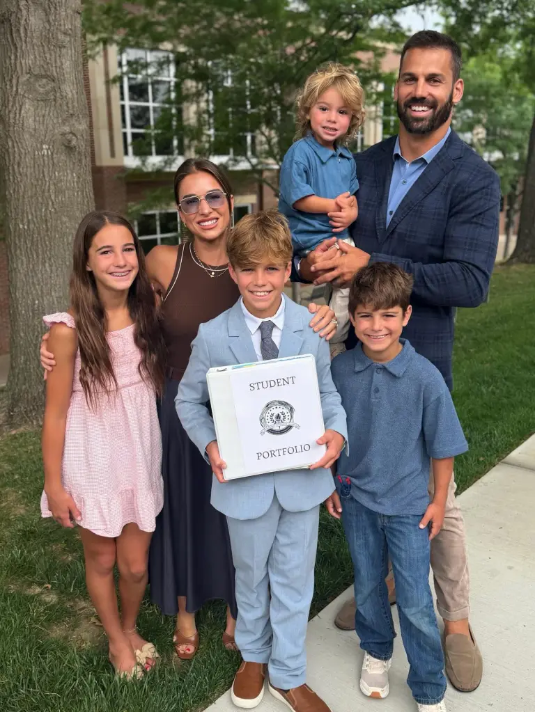 Jesse James and Eric Decker posing with their four children, one of whom holds a white binder labeled "Student Portfolio."