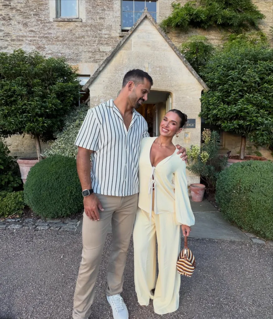 Jesse James and Eric Decker posing in front of a stone building with green foliage.