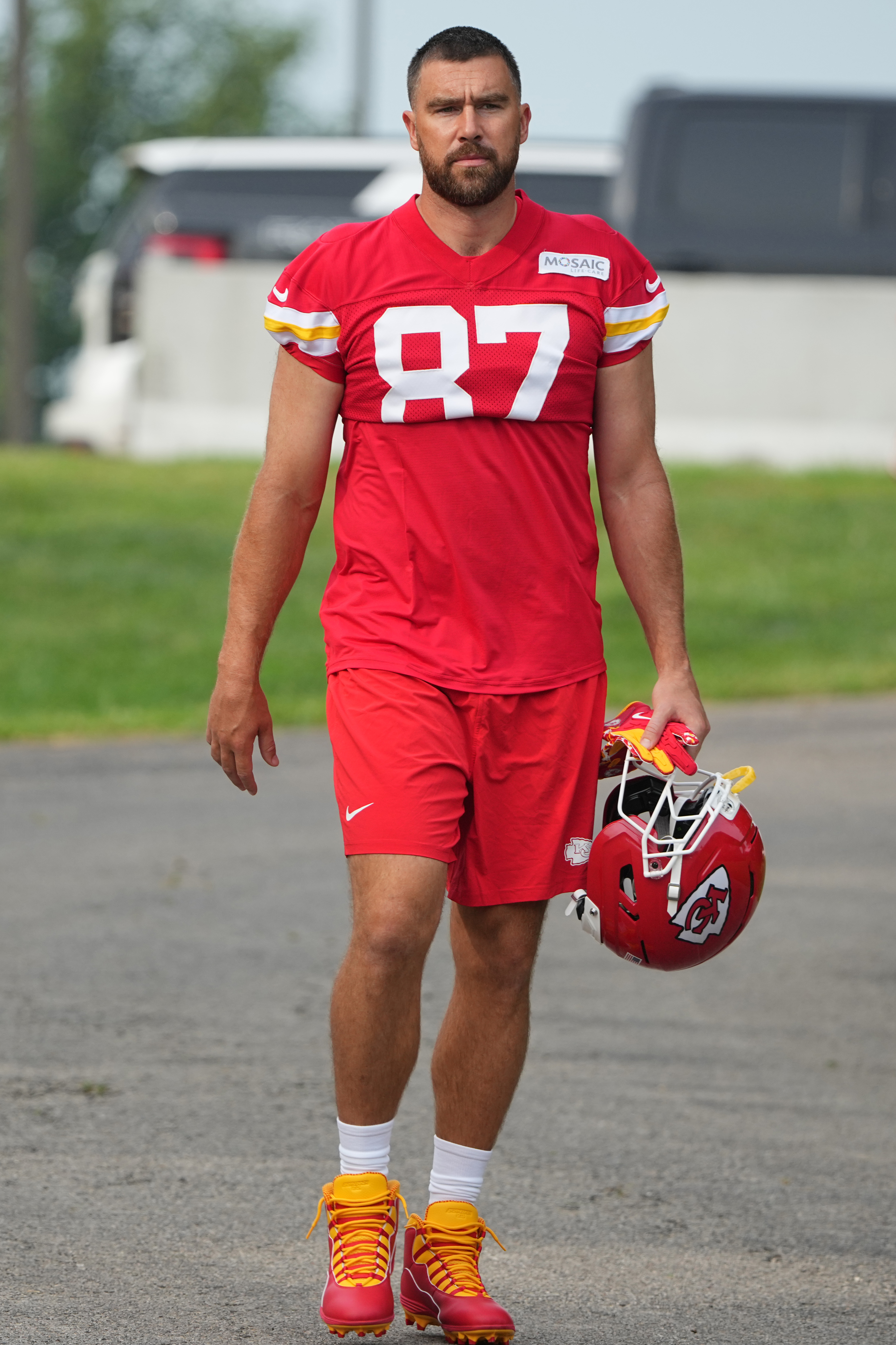 Travis Kelce in his Kansas City Chiefs uniform carrying a helmet and gloves during training camp.