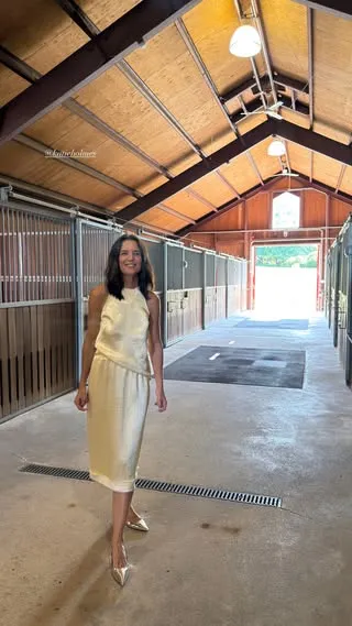 Katie Holmes in a cream-colored halter top and matching skirt in a stable.