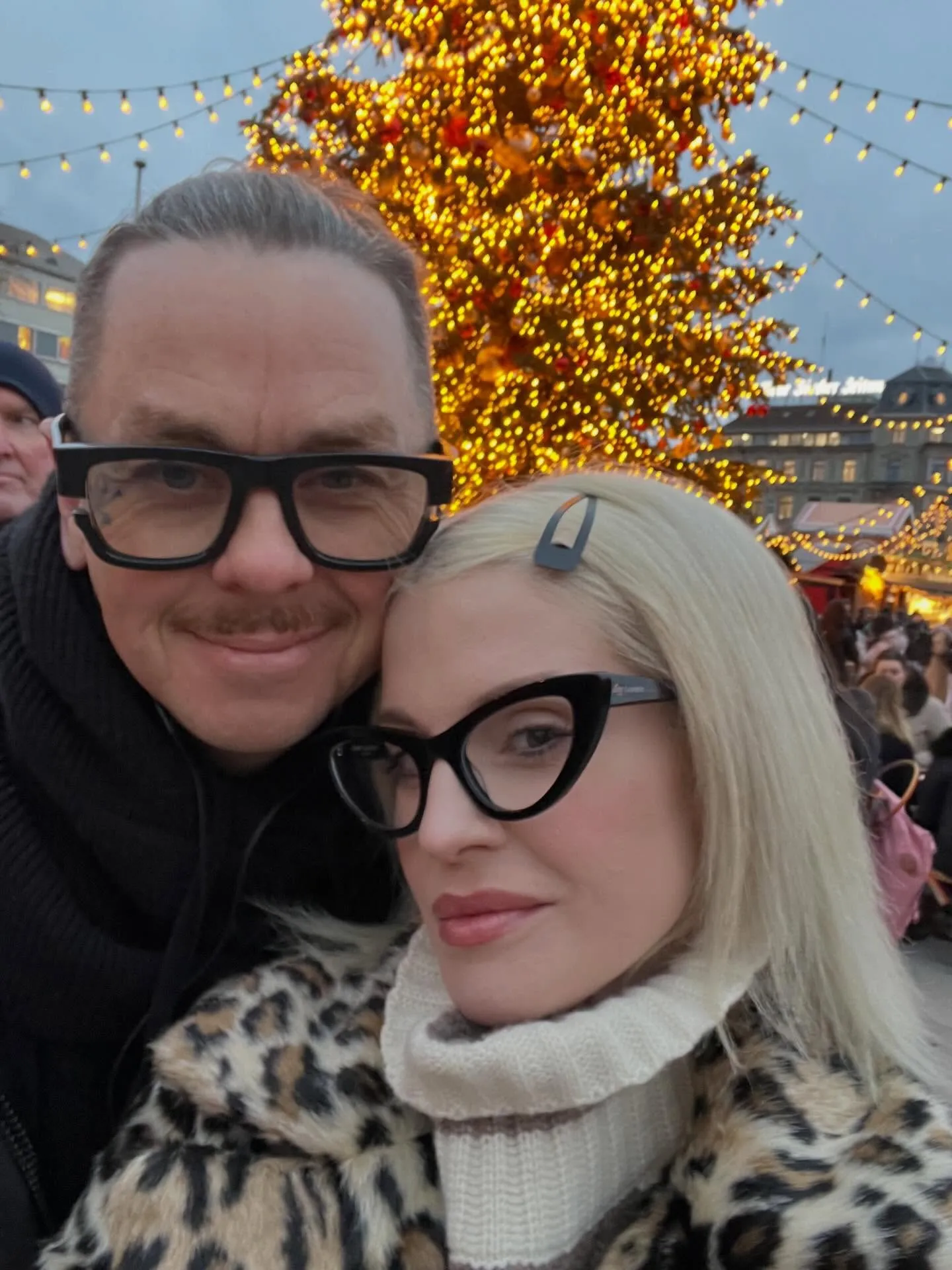 Kelly Osbourne and Sid Wilson posing for a selfie in front of a brightly lit Christmas tree.