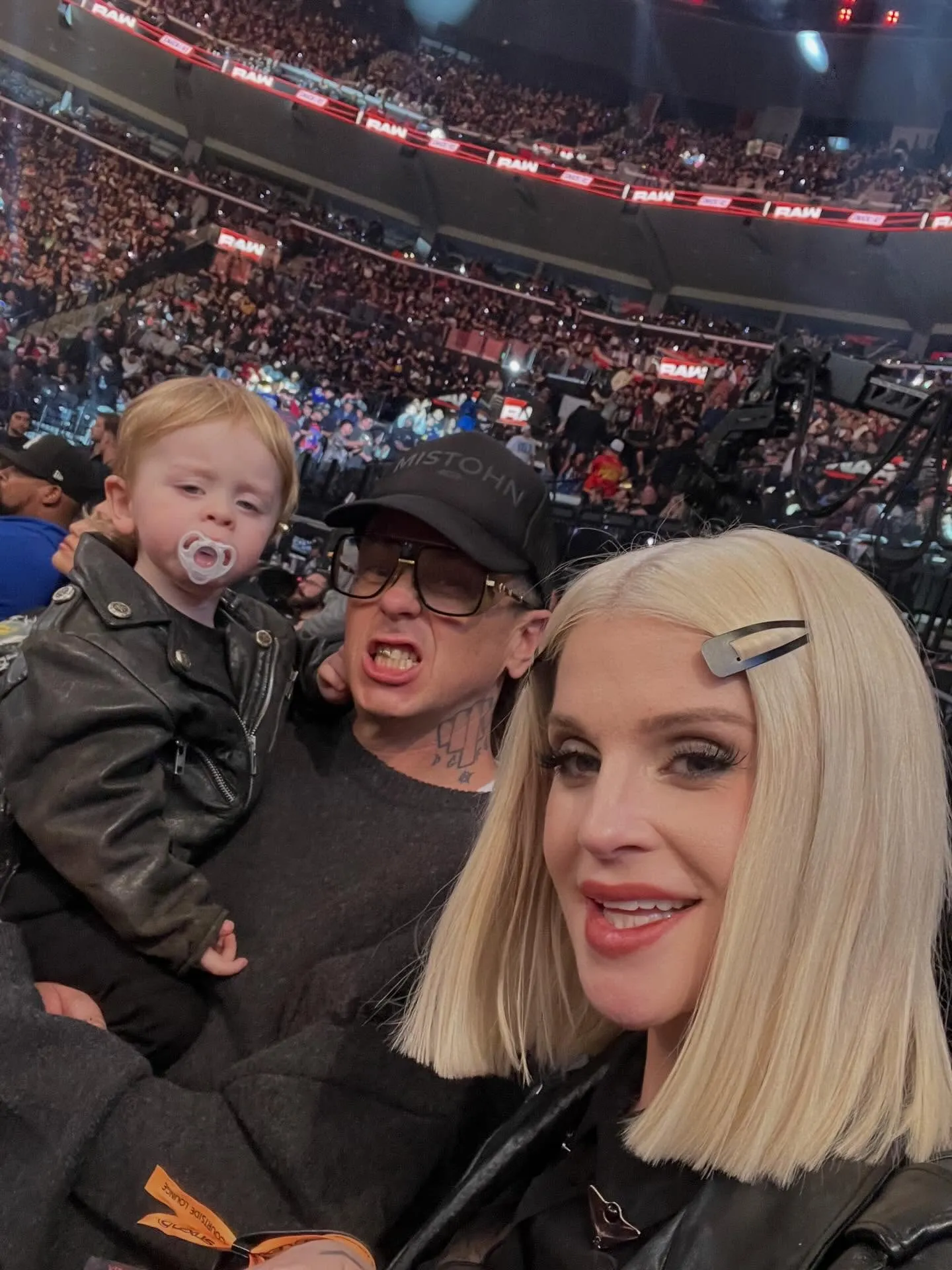 Kelly Osbourne and Sid Wilson with their child in a crowded arena.