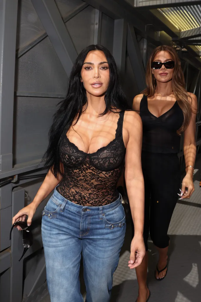 Kim Kardashian in a black lace bodysuit and jeans, walking with Khloe Kardashian in a black top and pants, both at the F1 Grand Prix of Monaco.