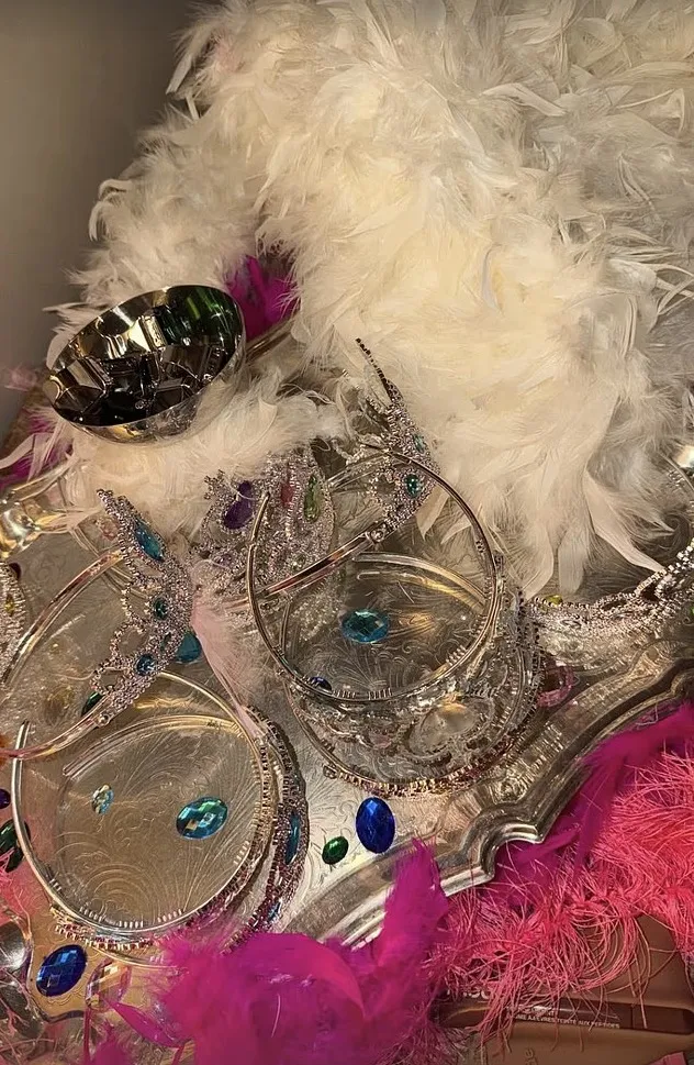 Silver tiaras with colorful jewels and white and pink feathers on a silver tray.