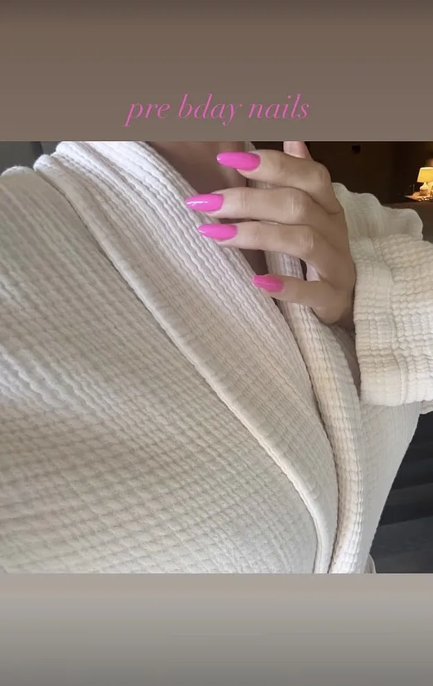 Kylie Jenner with long pink nails on a cream-colored bathrobe, with "pre bday nails" text.