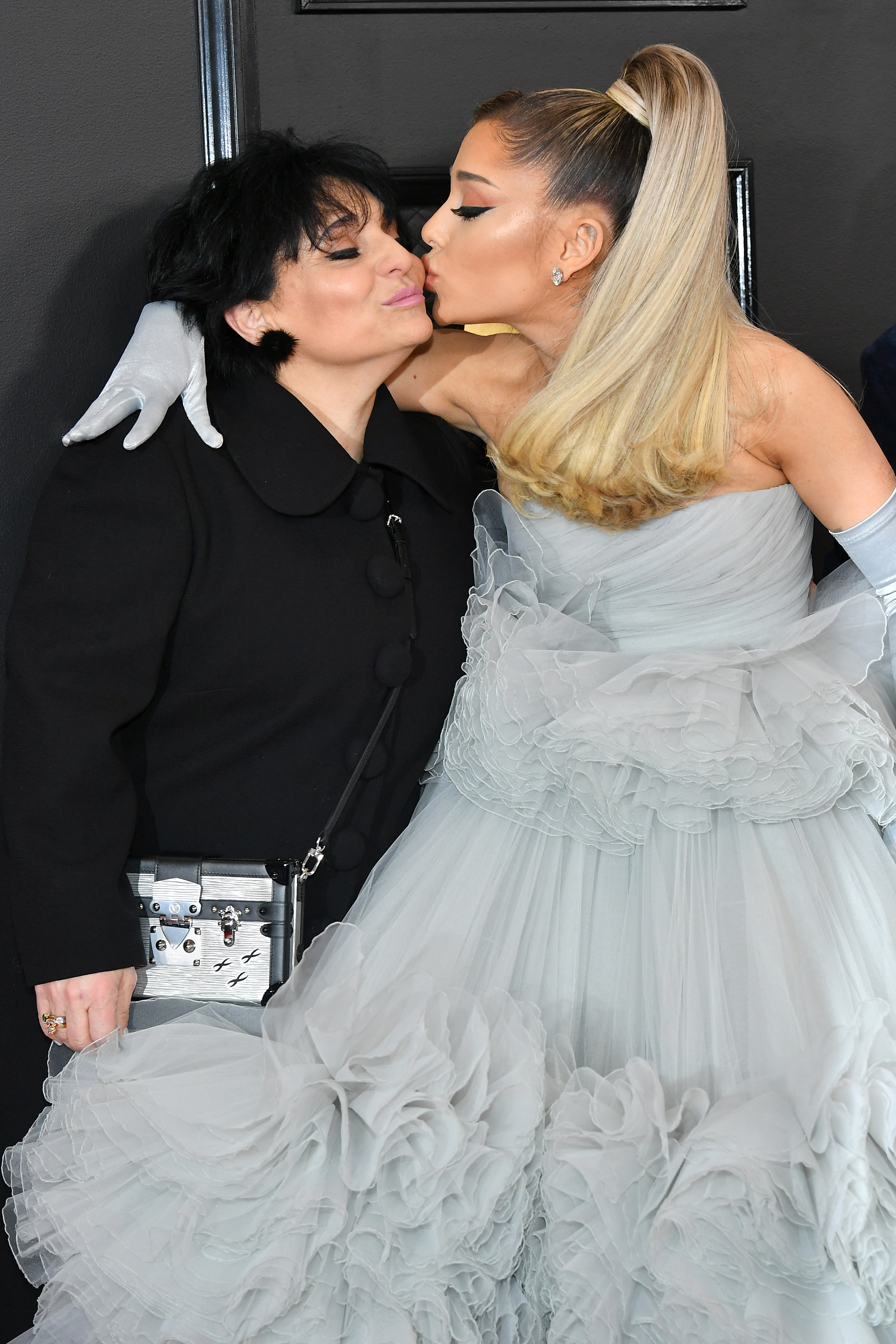 Ariana Grande, with blonde hair in a high ponytail and wearing a strapless light blue gown, kisses her mother, Joan Grande, on the cheek.