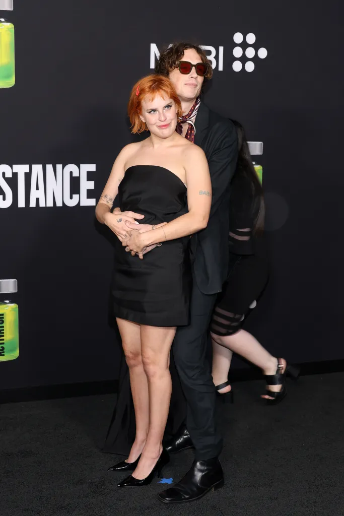 Tallulah Willis in a black strapless dress and Justin Acee in a black suit with a patterned scarf pose together at a movie premiere.