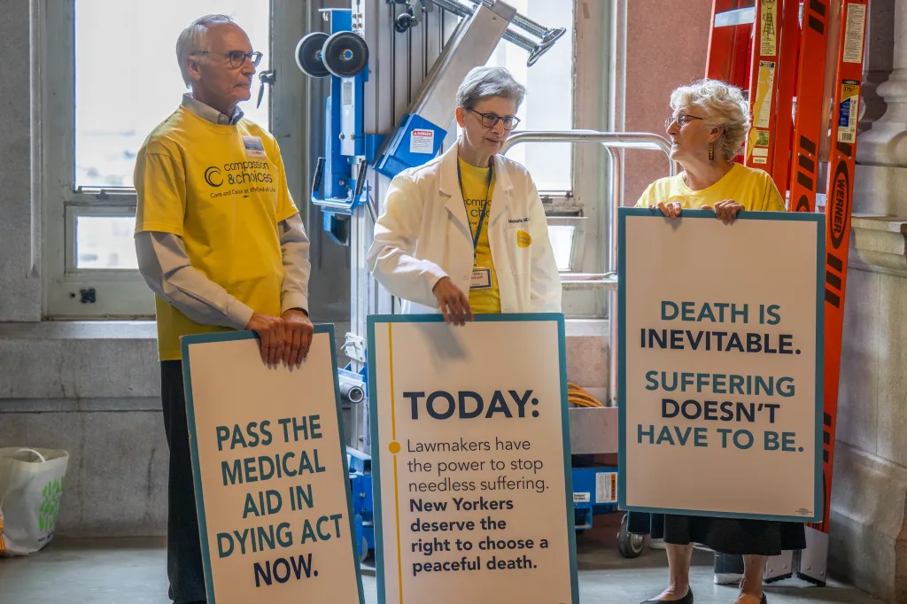 Thad Mirer, Dr. Mary Applegate, and Deborah Vogel advocate for the Medical Aid in Dying Act with signs at the state Capitol in Albany, N.Y.