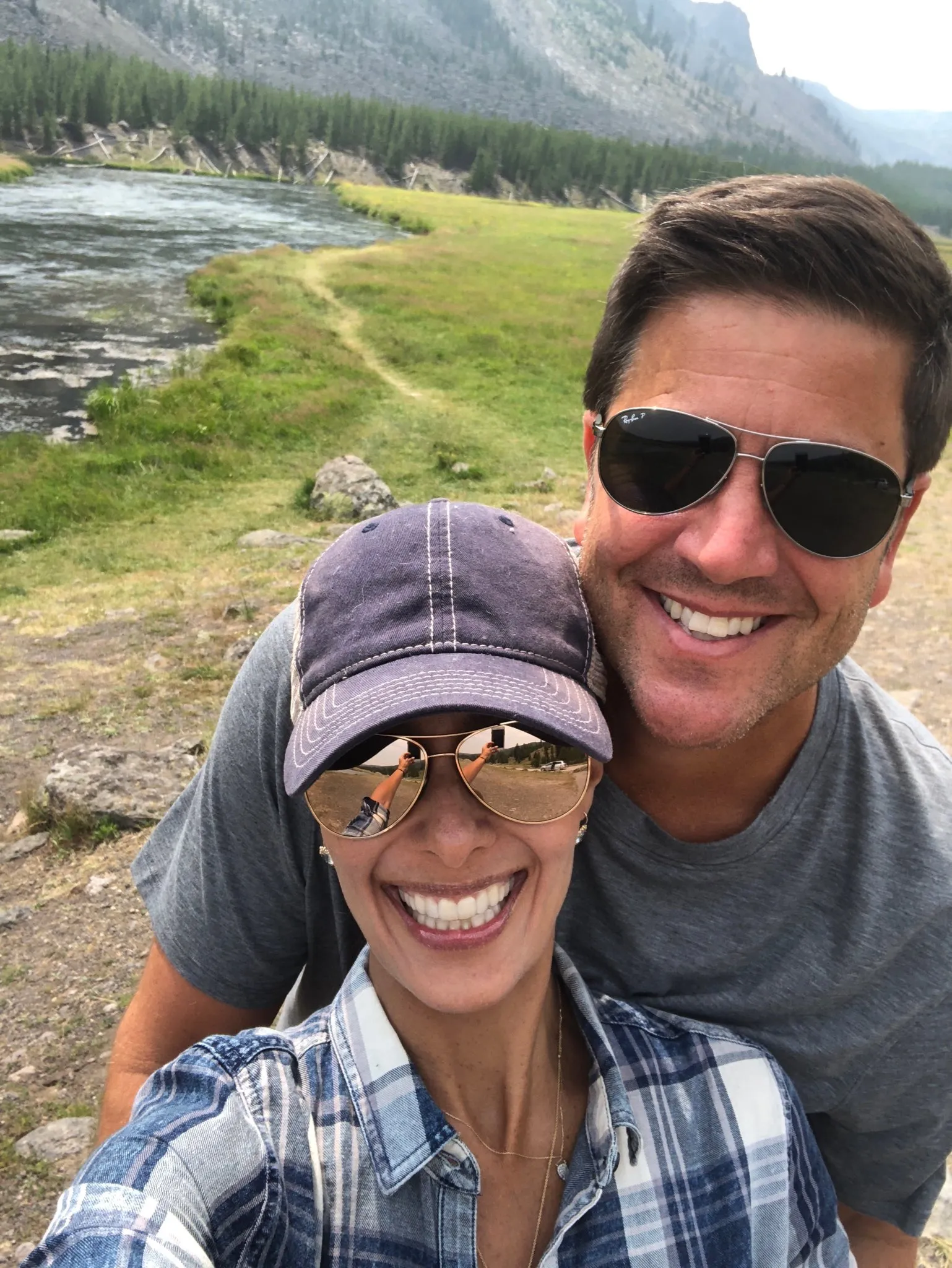 Liz Cho and Josh Elliott posing for a photo in a natural setting with a river and mountains in the background.