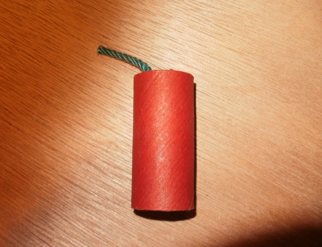 M-80 firecracker with a green fuse on a wooden surface.