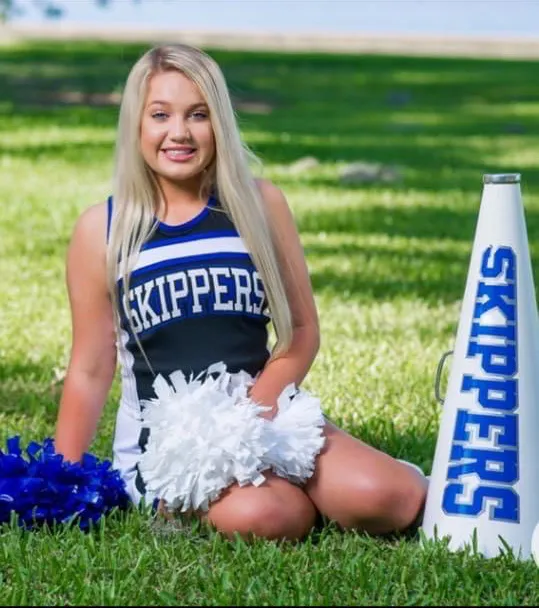 Madison Brooks in a cheerleading uniform, holding white pom-poms, next to a megaphone.