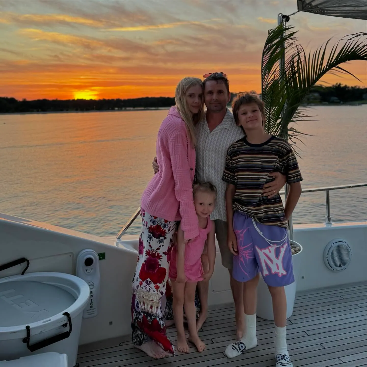 Matt Bellamy, Elle Evans, and their two children pose on a boat at sunset.