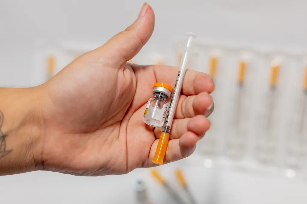 Hand holding a vial of tirzepatide medication and an insulin syringe for weight loss and diabetes treatment.