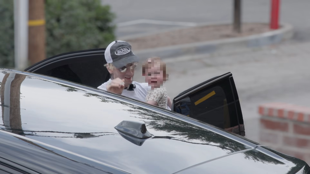 Machine Gun Kelly holding his daughter Saga in the doorway of a car.