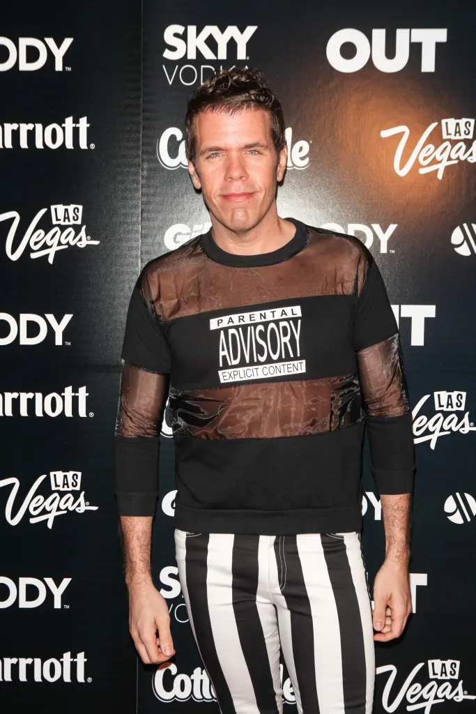 Perez Hilton at an event wearing a sheer "Parental Advisory" shirt and black and white striped pants.