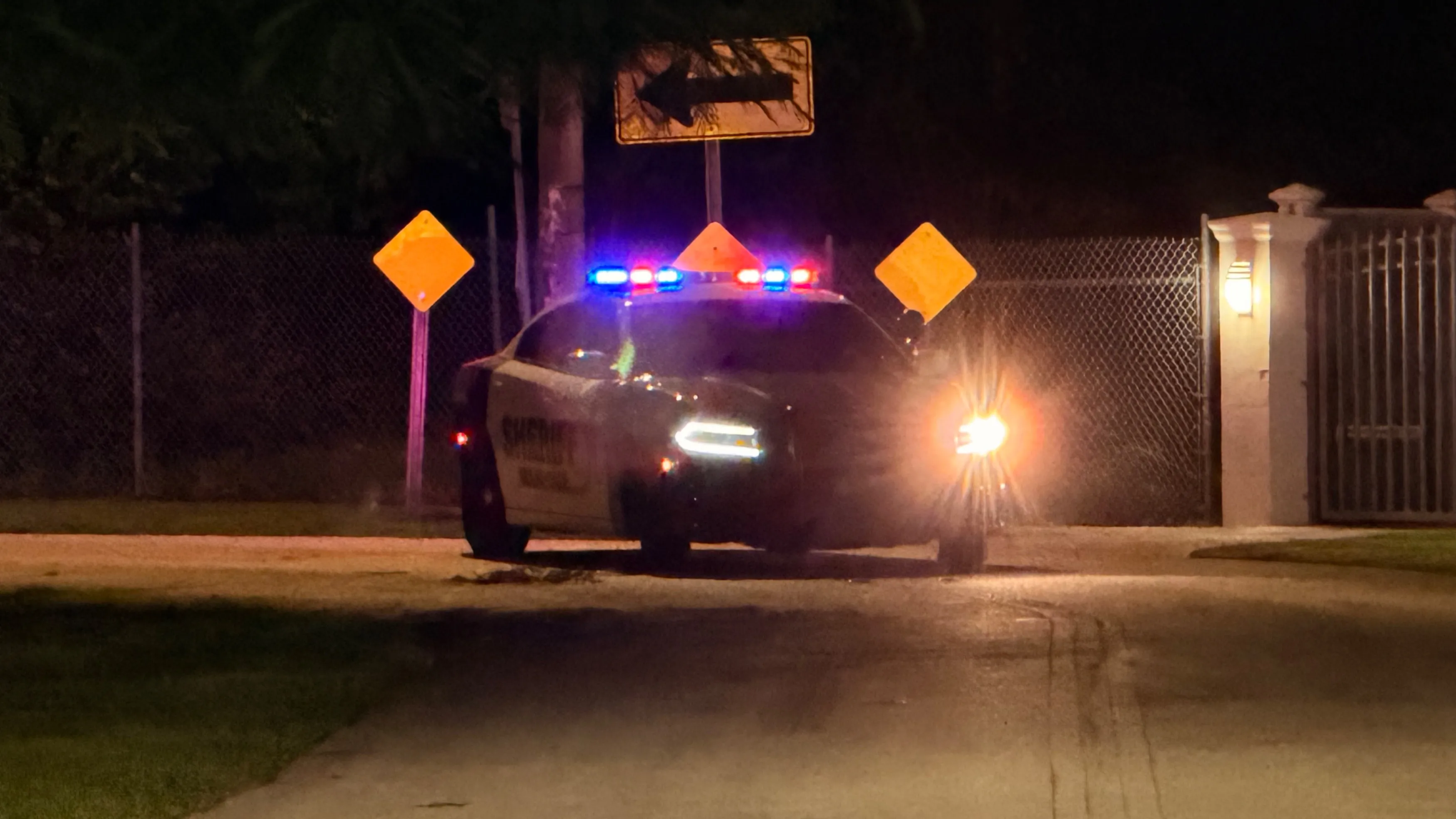 Police vehicle with flashing blue and red lights parked outside a Miami neighborhood.