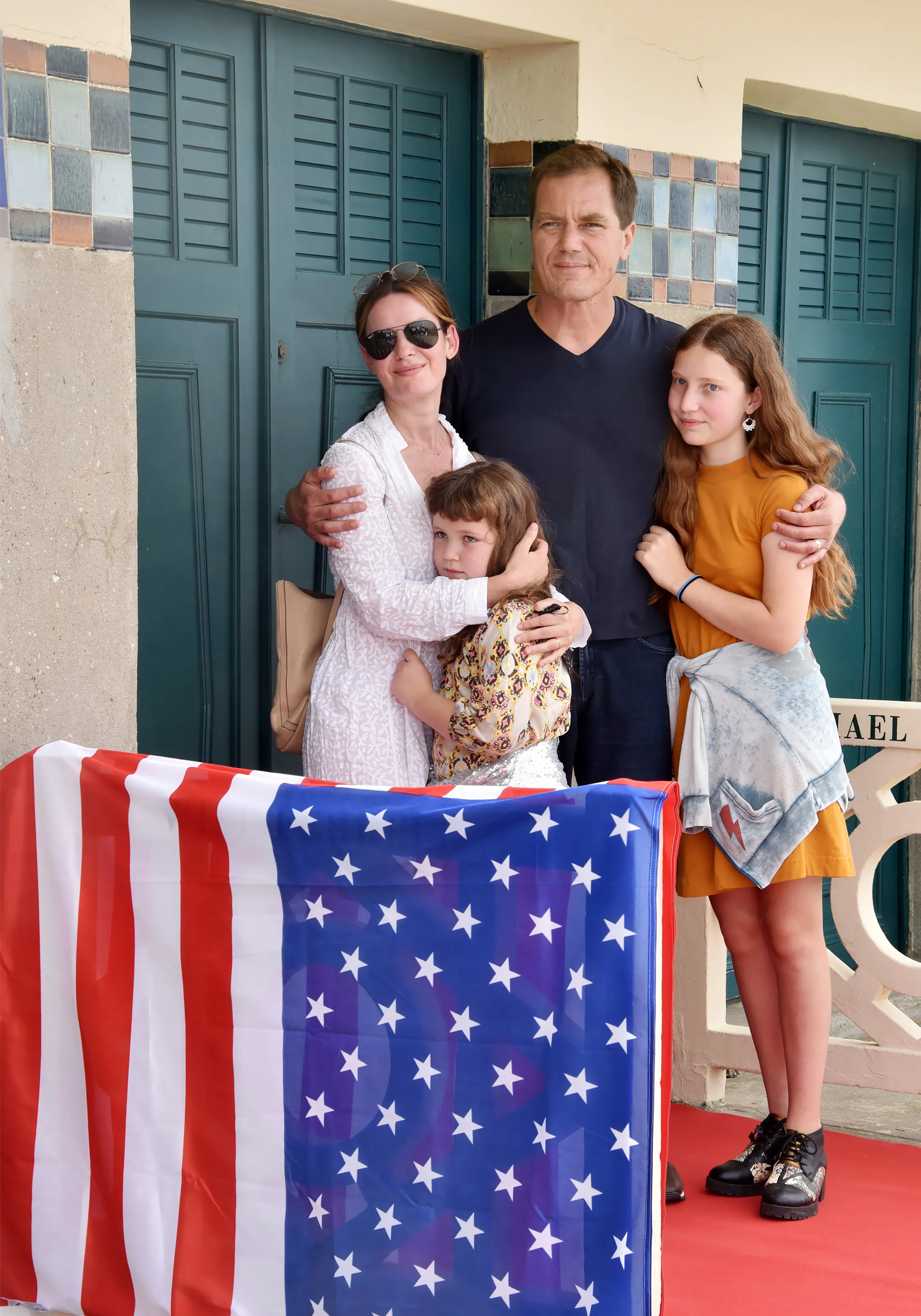 Michael Shannon, his wife Kate Arrington, and their two daughters stand behind an American flag banner.