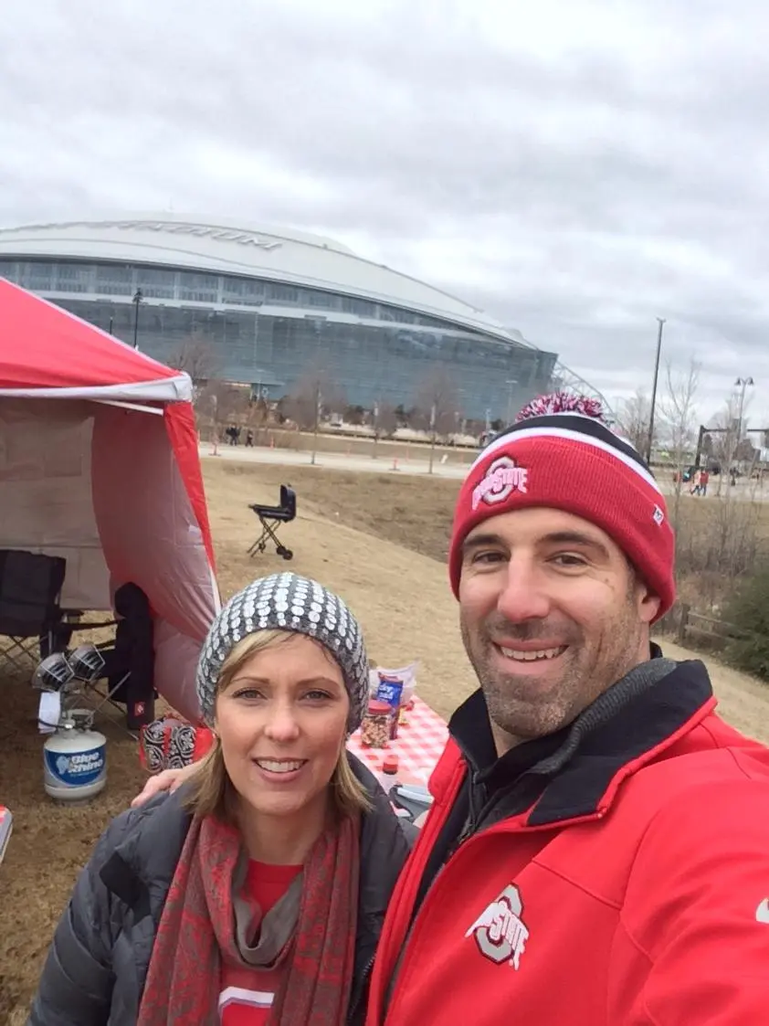 Mike Vrabel and wife Jen at a tailgate with a stadium in the background.