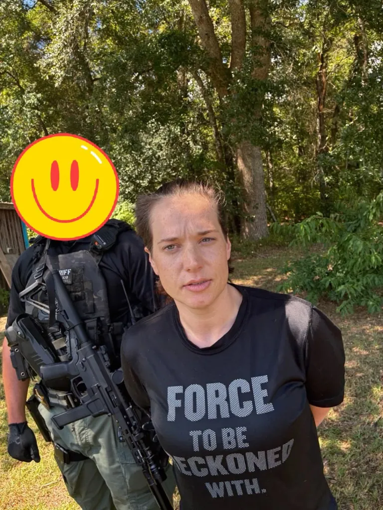 Isabelle Johnson, murder suspect, in handcuffs, standing in front of a police officer and trees.