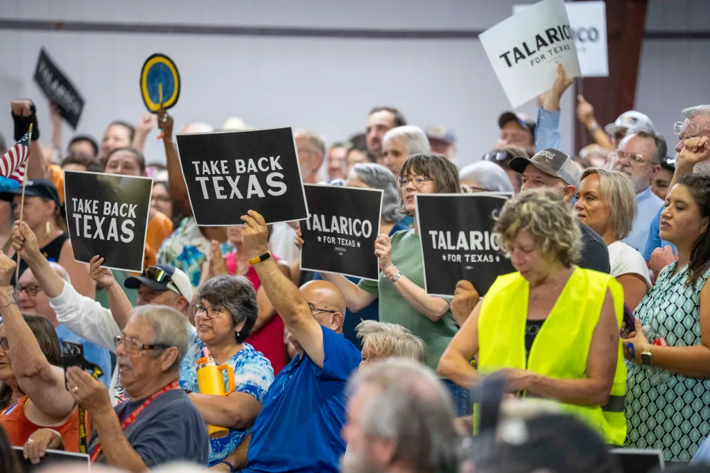 Supporters at a James Talarico campaign rally in Lockhart, Texas, hold up signs that read "TAKE BACK TEXAS" and "TALARICO * FOR TEXAS *".