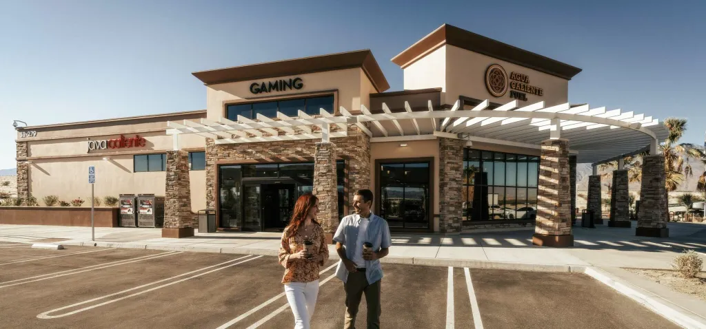 Agua Caliente Fuel gas station building with signs for "Gaming" and "Java Caliente," with two people walking in the foreground.