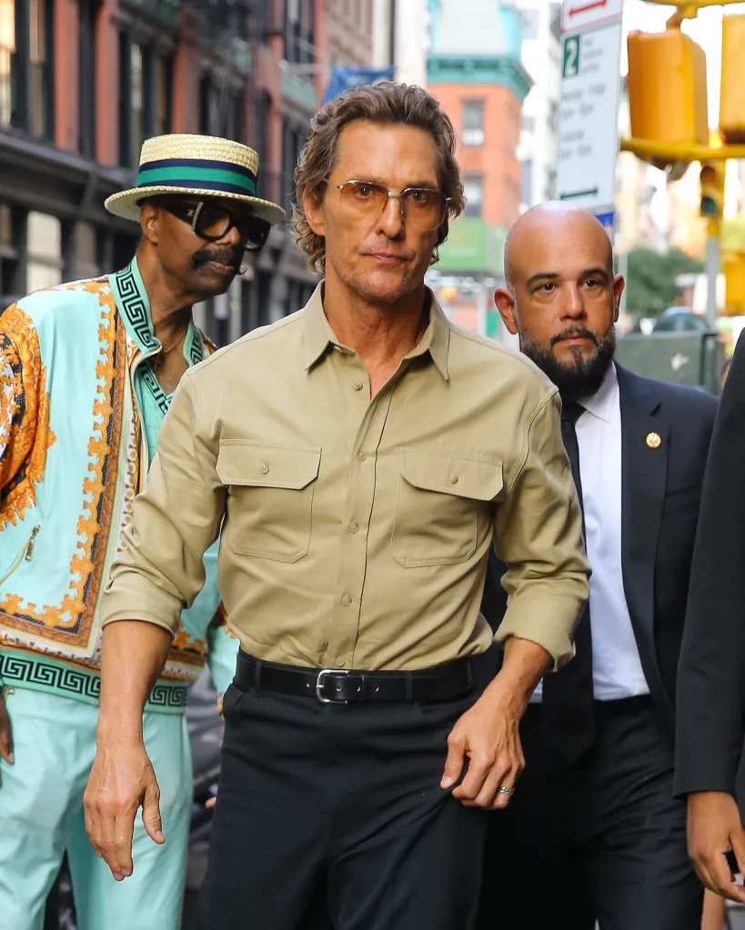 Matthew McConaughey walking on a New York City street with two men, one in a straw hat and sunglasses, and another in a suit.