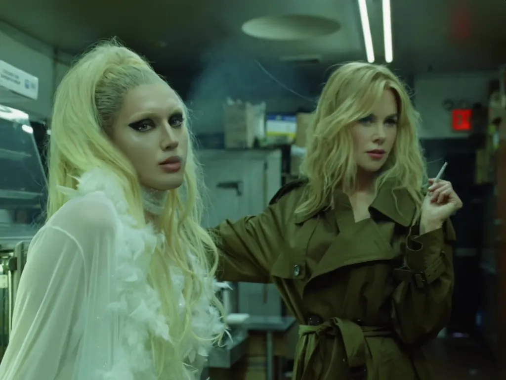 Nicole Kidman in a trench coat holding a cigarette next to Troye Sivan in drag.