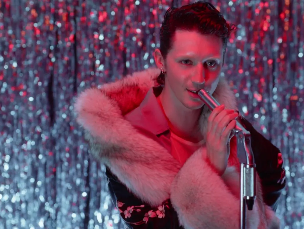 Troye Sivan in a fur-trimmed coat, holding a microphone.
