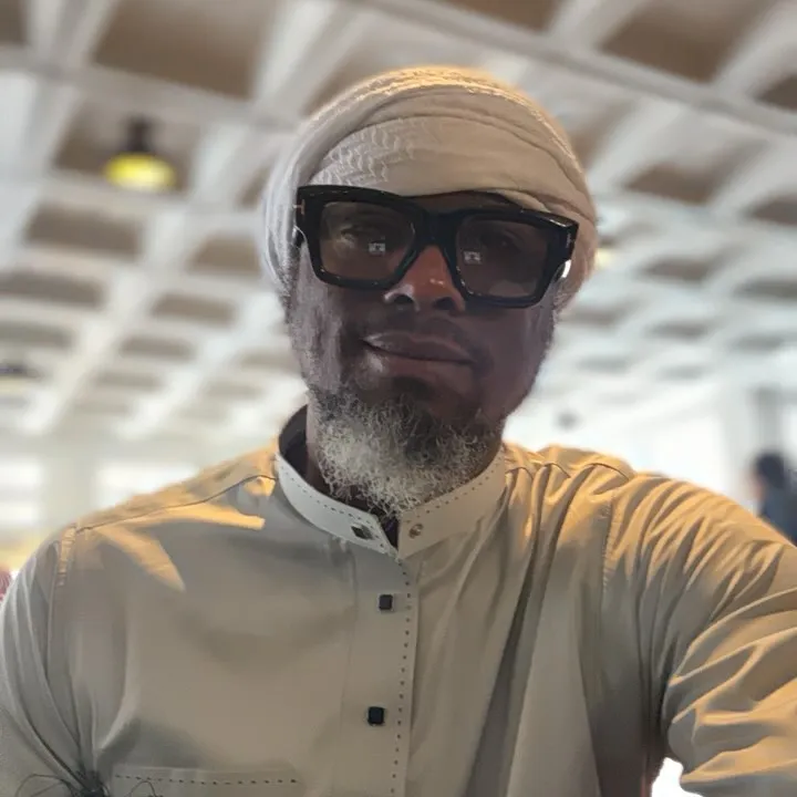 Man wearing a head wrap, glasses, and a long-sleeved shirt with a high collar.