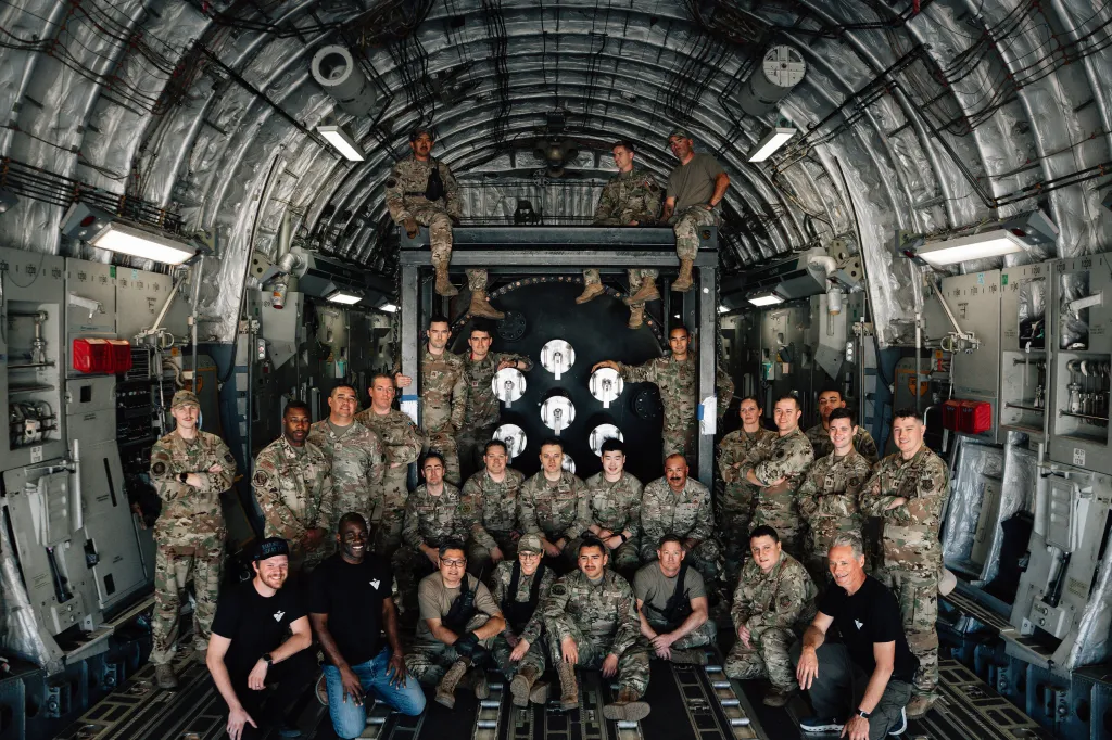 A group of 28 uniformed military personnel and civilians pose for a photo inside a cargo plane.