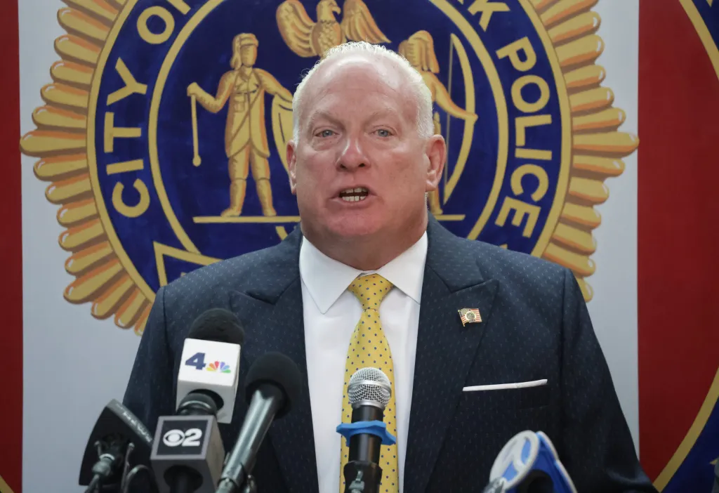 Scott Munro speaking at a podium with microphones in front of a New York City Police Department seal.