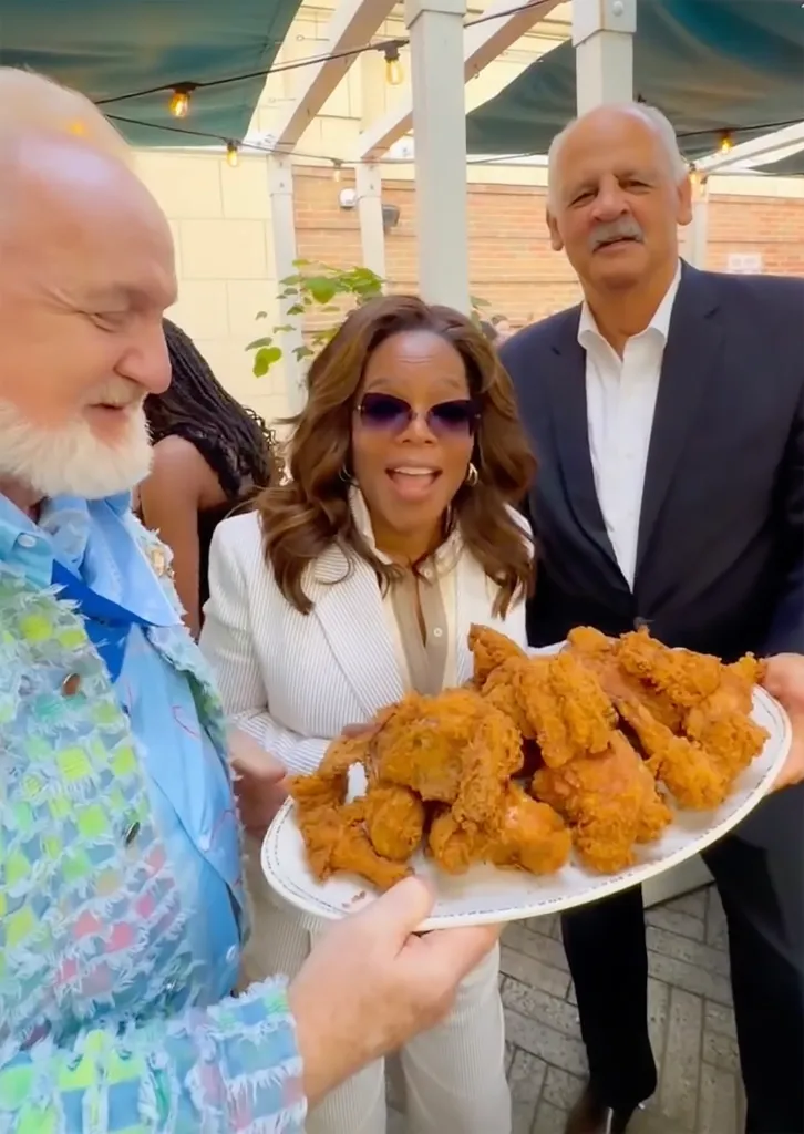 Oprah Winfrey and Stedman Graham smiling at a man holding a platter of fried chicken.