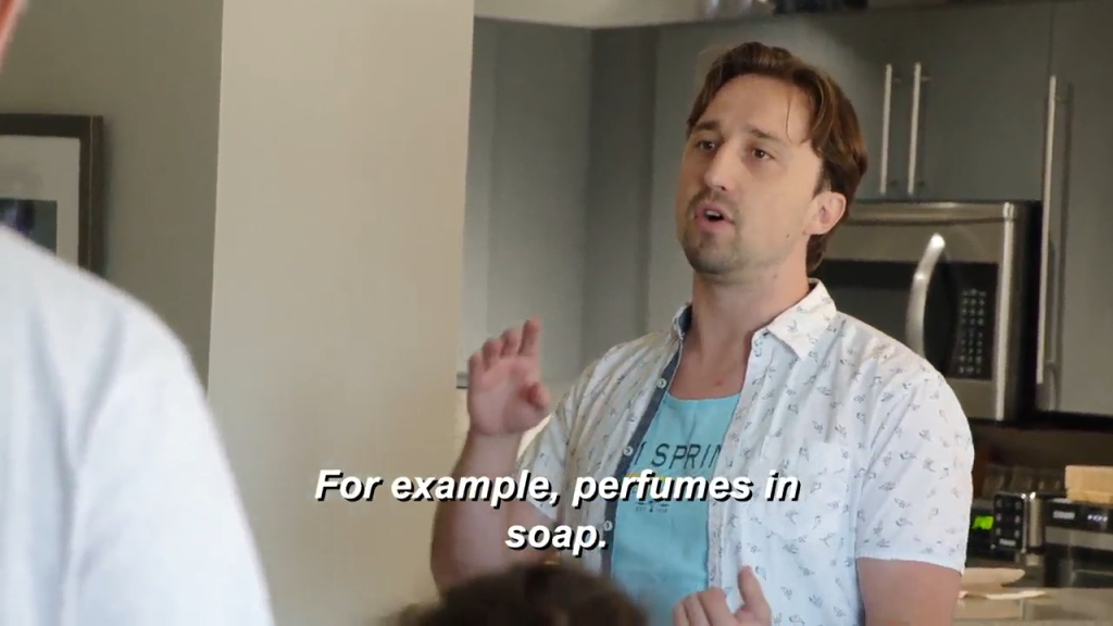 A man wearing a patterned short-sleeved shirt and a light blue t-shirt speaks with text overlayed, "For example, perfumes in soap:".