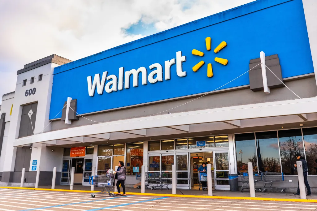 Exterior of a Walmart store with shoppers and shopping carts outside the entrance.