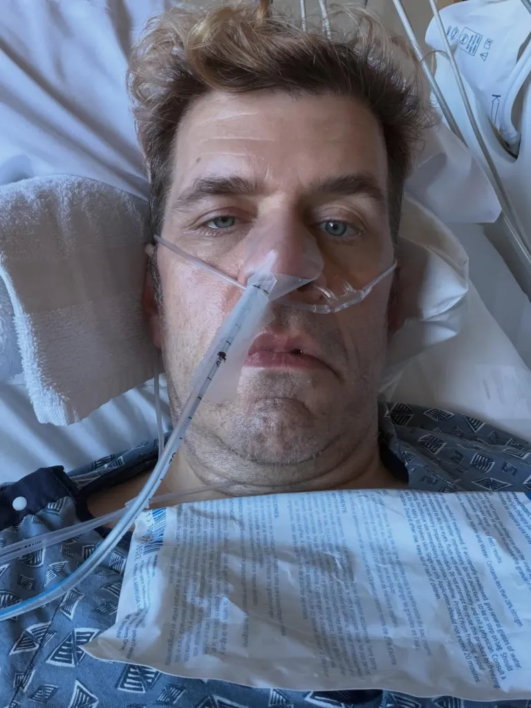 Perez Hilton lies in a hospital bed with a nasal cannula.