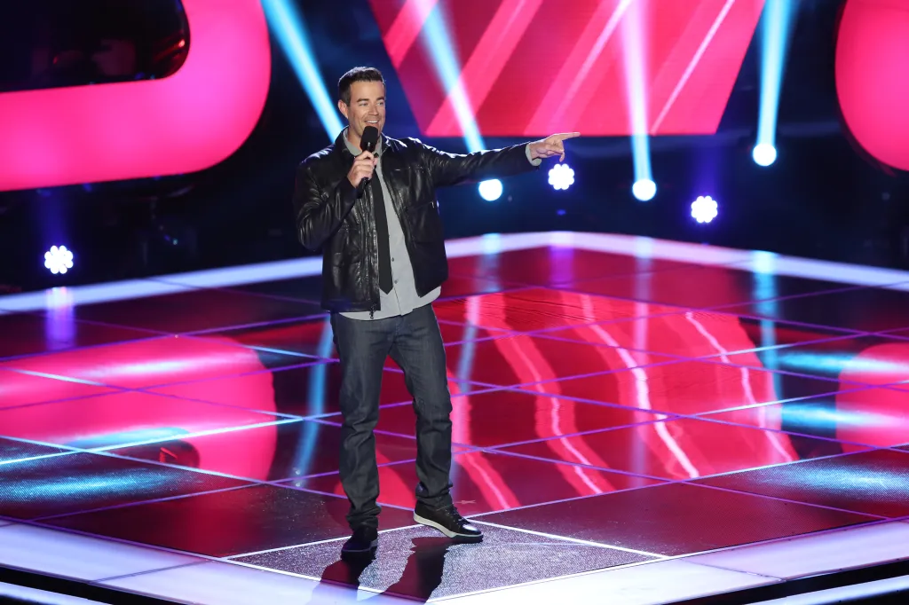 Carson Daly holding a microphone and pointing on stage.