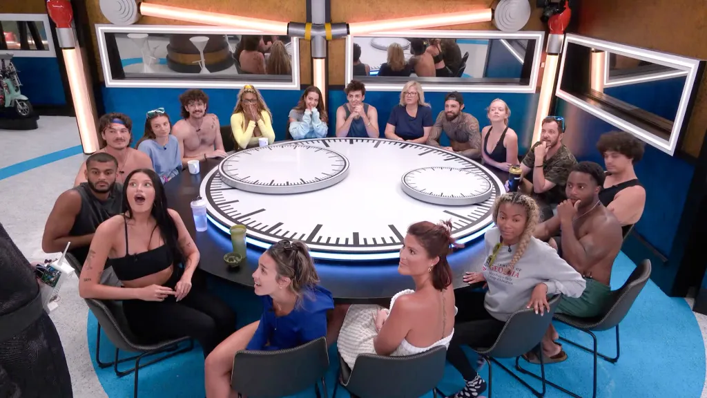 The Big Brother cast of 17 contestants sitting around a large round table with clock faces.